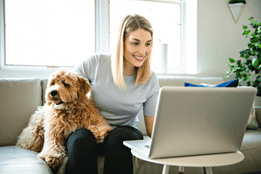 A woman at a desk with two dogs beside her, working on a laptop, creating a cozy home office atmosphere.