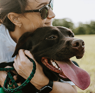 A woman embraces her dog in a vast grassy field, displaying the bond between a pet owner and her furry companion.