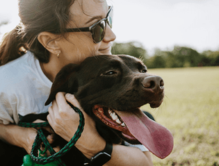 A woman embraces her dog in a vast grassy field, displaying the bond between a pet owner and her furry companion.